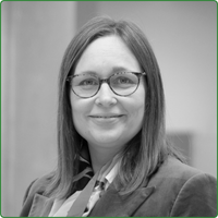 A black and white head shot of Anika Ervin-Ward. She wears glasses and is standing in an office space