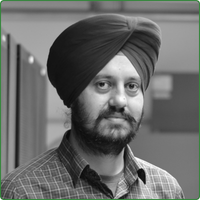 A black and white head shot of Harpinder Singh, standing in an office space and next to him is a row of network servers